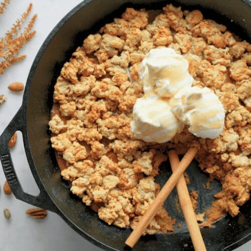 Sourdough pumpkin cobbler in cast iron skillet with cinnamon sticks and vanilla ice cream