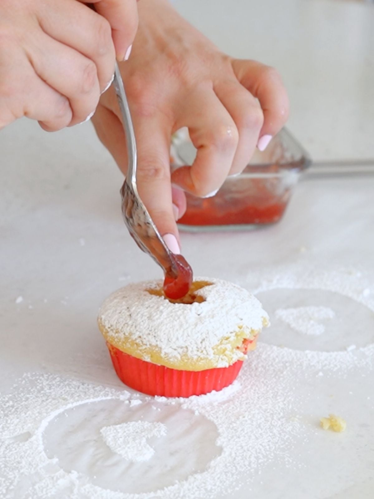 A spoonful of jam being placed into the heart cupcake cutout.