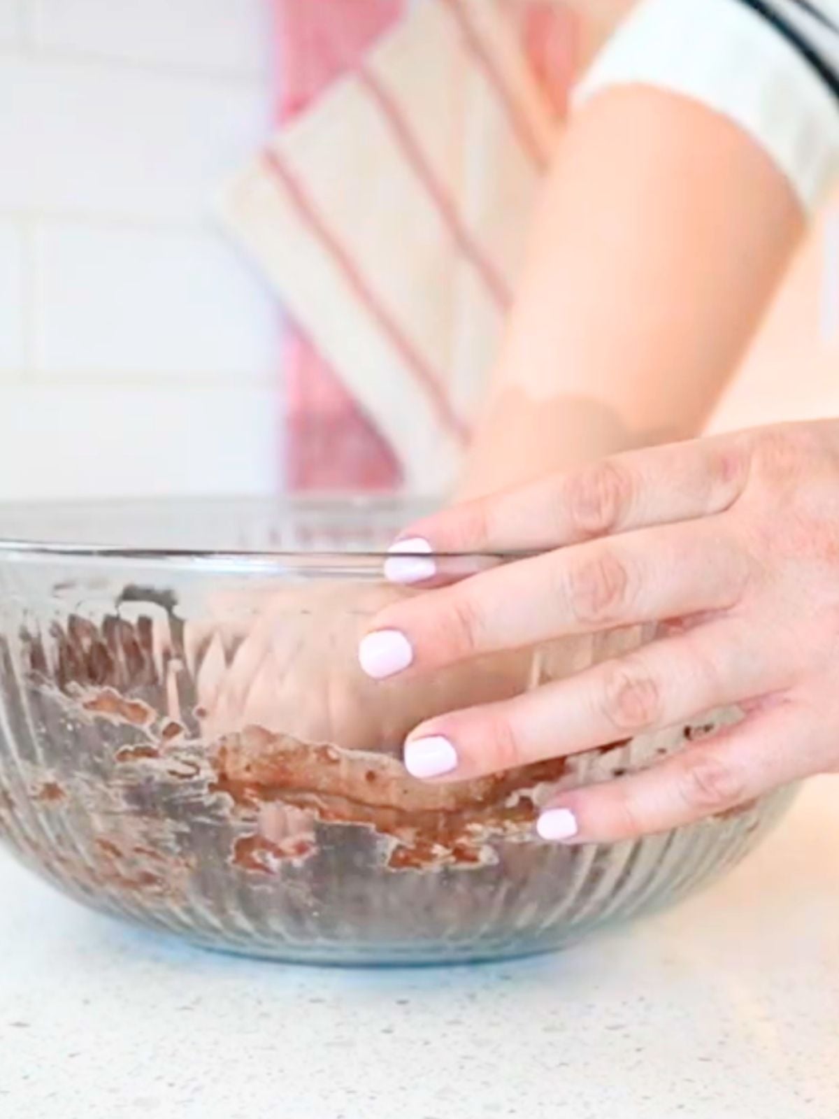 Hands mixing dough in a glass bowl.