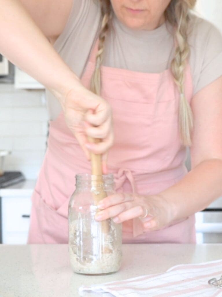 Woman stirring sourdough starter in a jar.