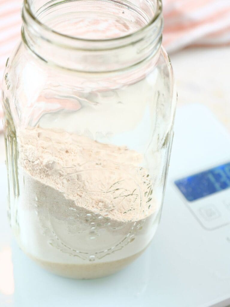 A jar of flour and water on a kitchen scale.