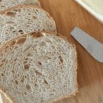 Sourdough sandwich bread on wood tray with butter knife and butter