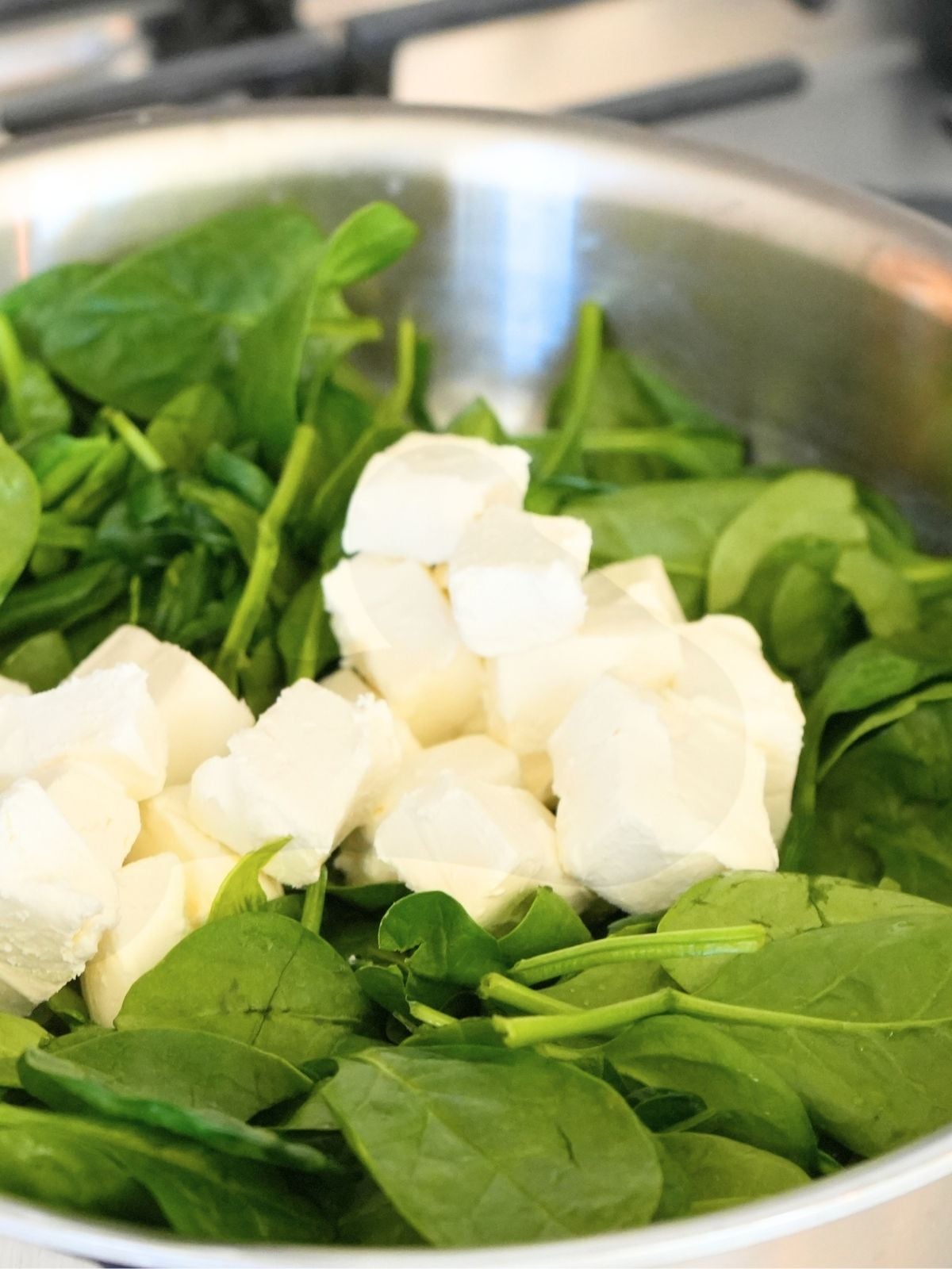 Cream cheese on top of spinach in a skillet.