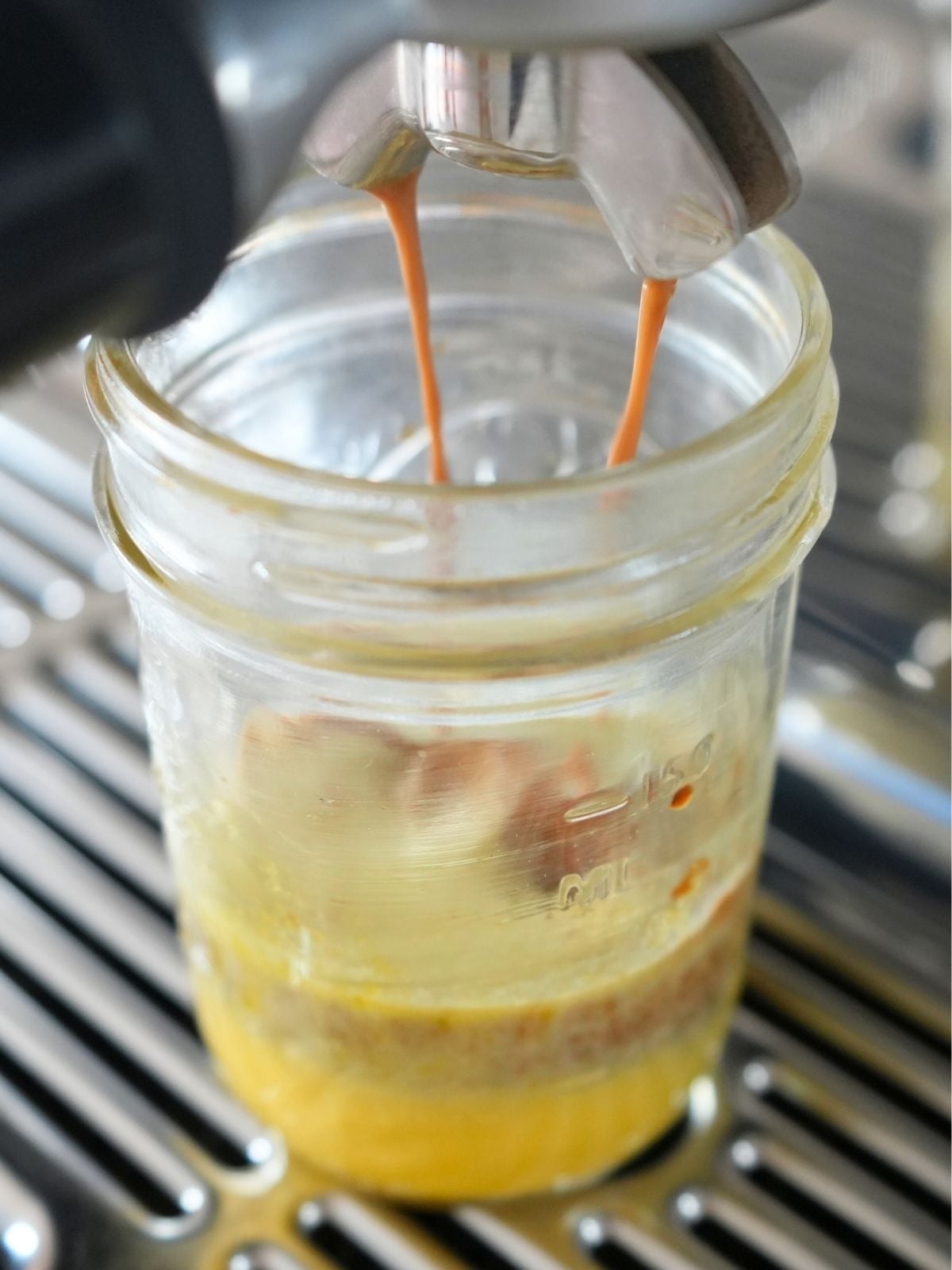 Coffee from espresso machine pouring into jar with egg yolk mixture.