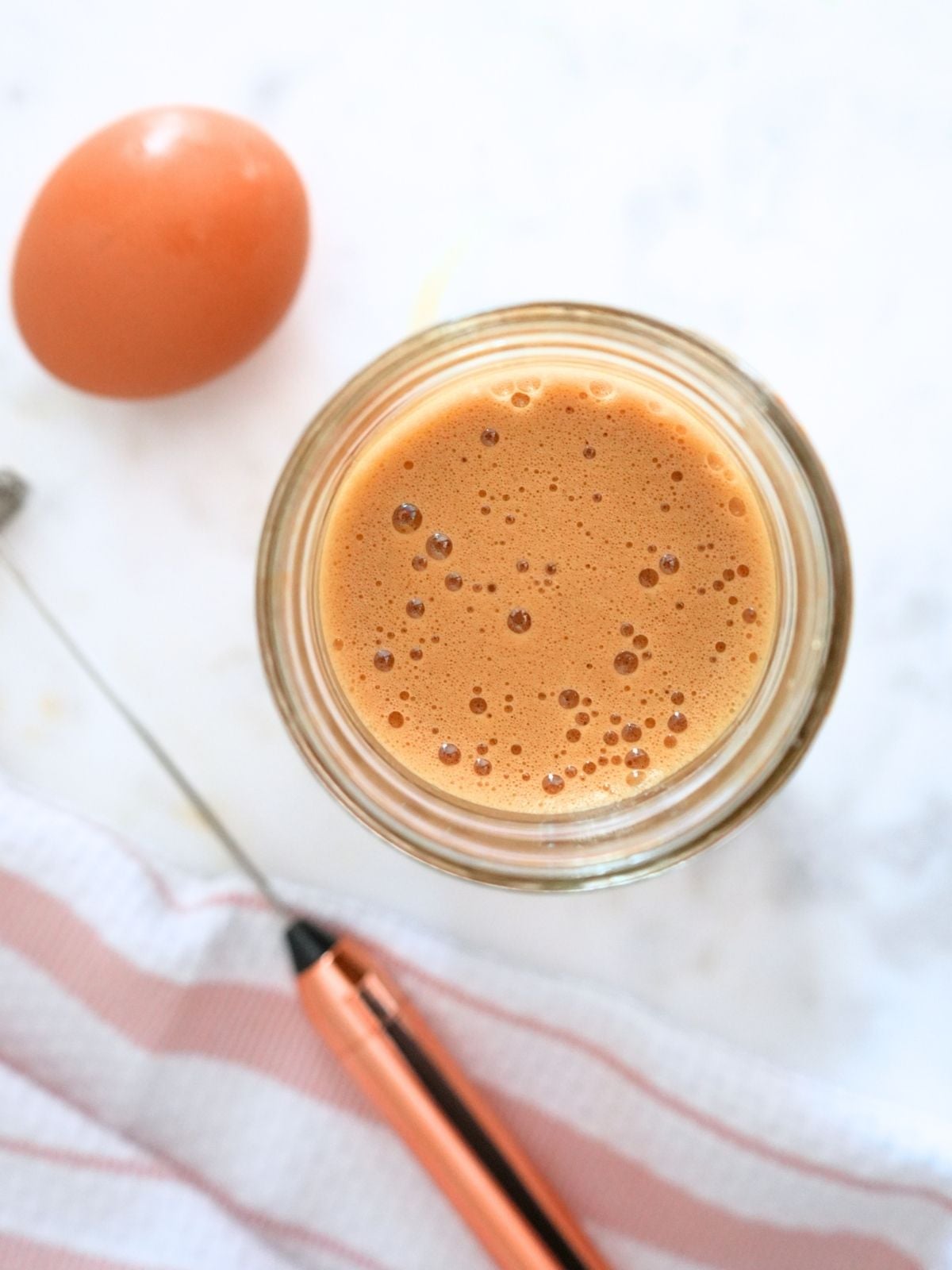 Egg yolk coffee in a mason jar next to a frother and whole egg.