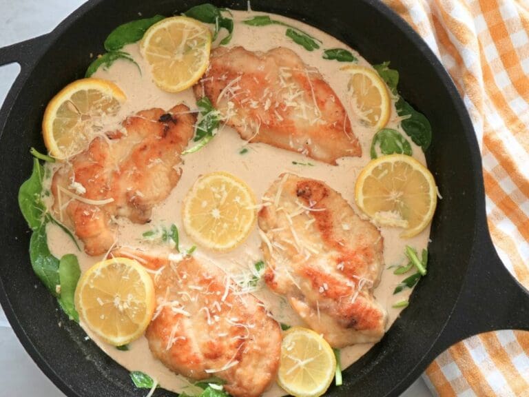 Creamy lemon chicken in cast iron skillet, next to a decorative towel.