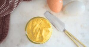 A small jar of French mayonnaise next to a knife and fresh eggs
