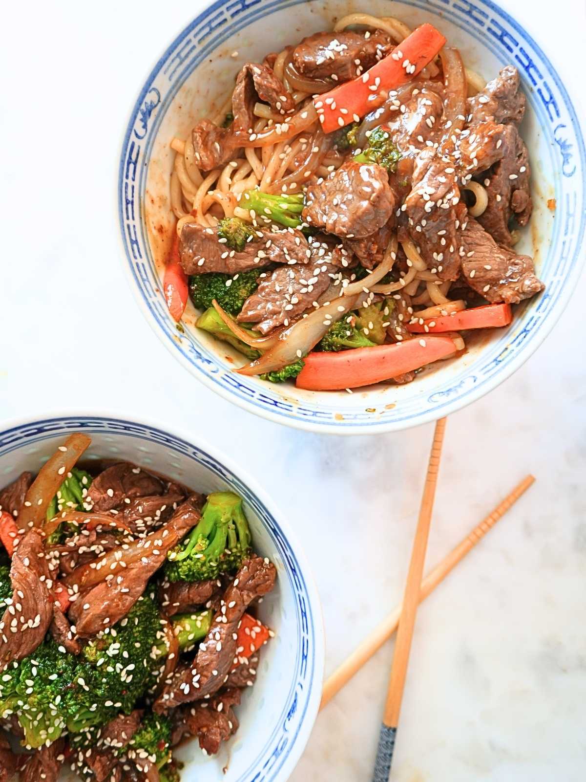 Two bowls of beef and broccoli over rice and noodles.