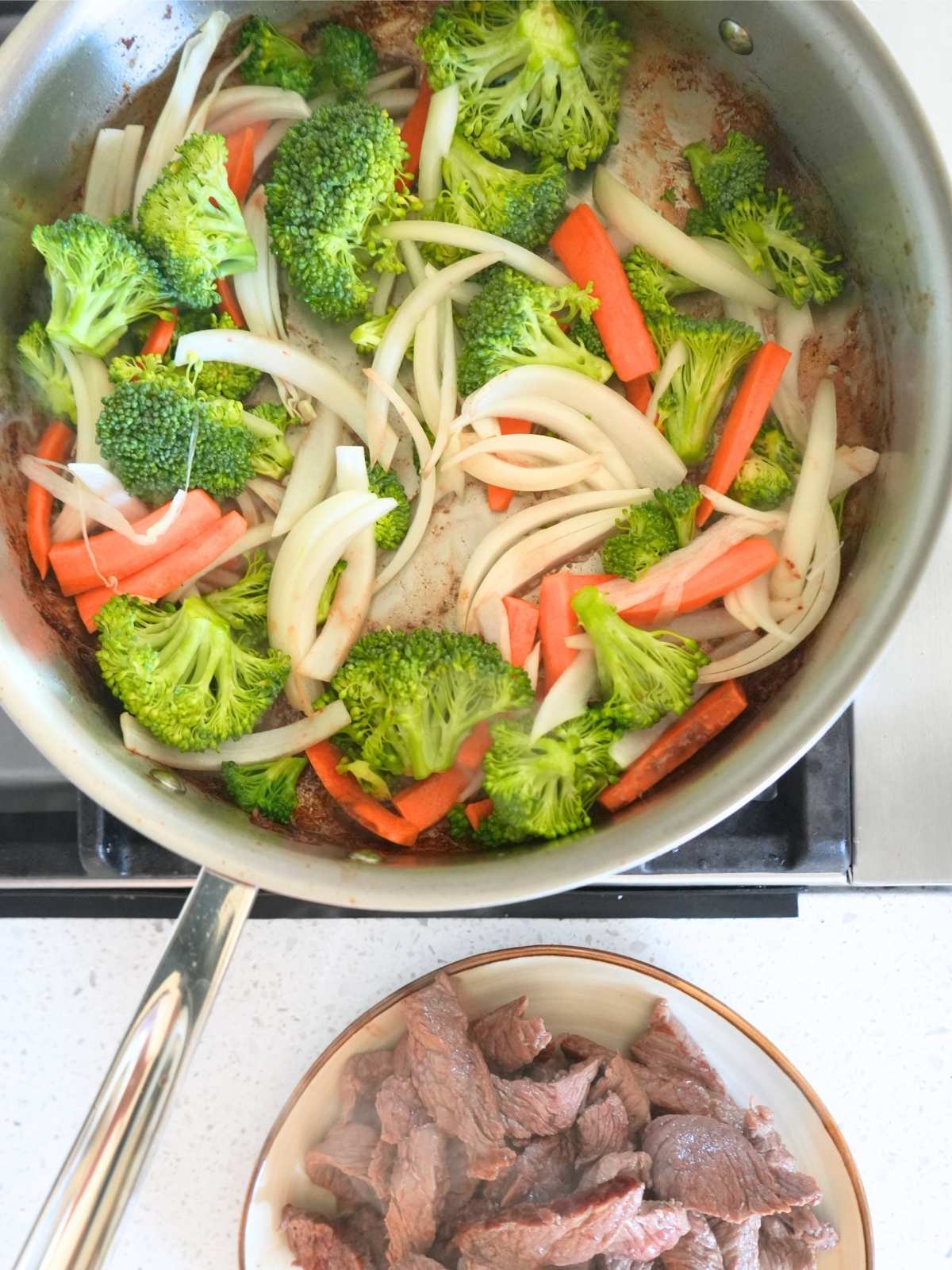 Veggies cooking in a skillet with steak.