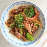 Beef and broccoli in bowl with chop sticks.