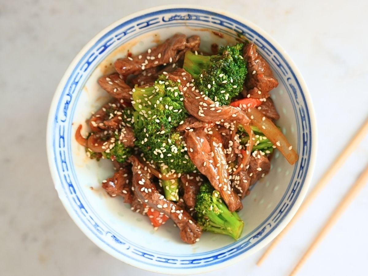 Beef and broccoli in bowl with chop sticks.