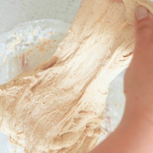 Hands stretching sourdough dough out a glass bowl