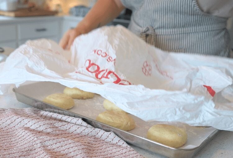 Woman covering sourdough burger bun dough with plastic