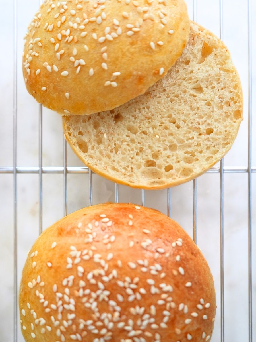 Two sourdough burger buns on a cooling rack, one sliced open to show the tender crumb