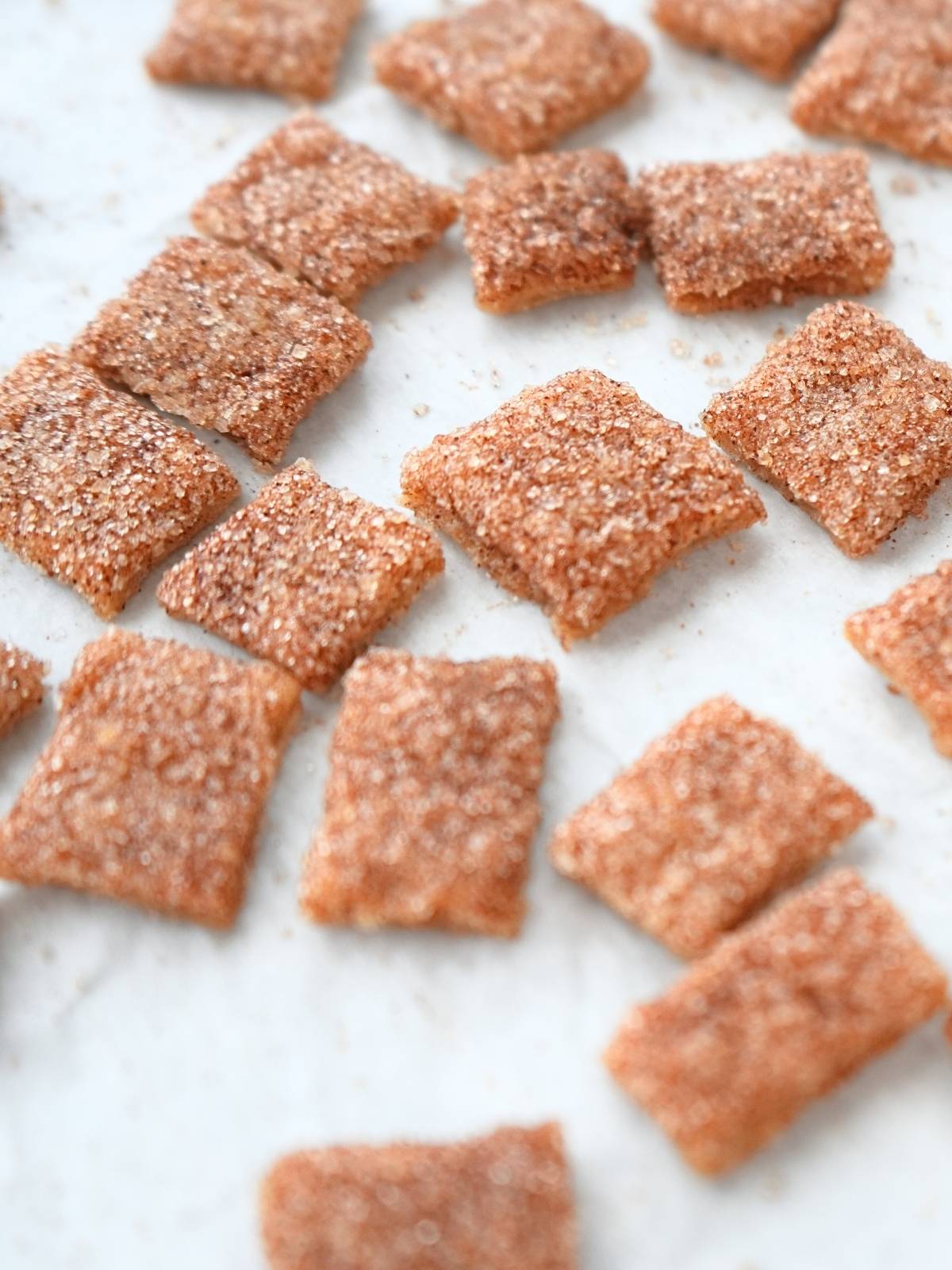 Baked squares of sourdough discard Cinnamon Toast Crunch scattered on a counter.