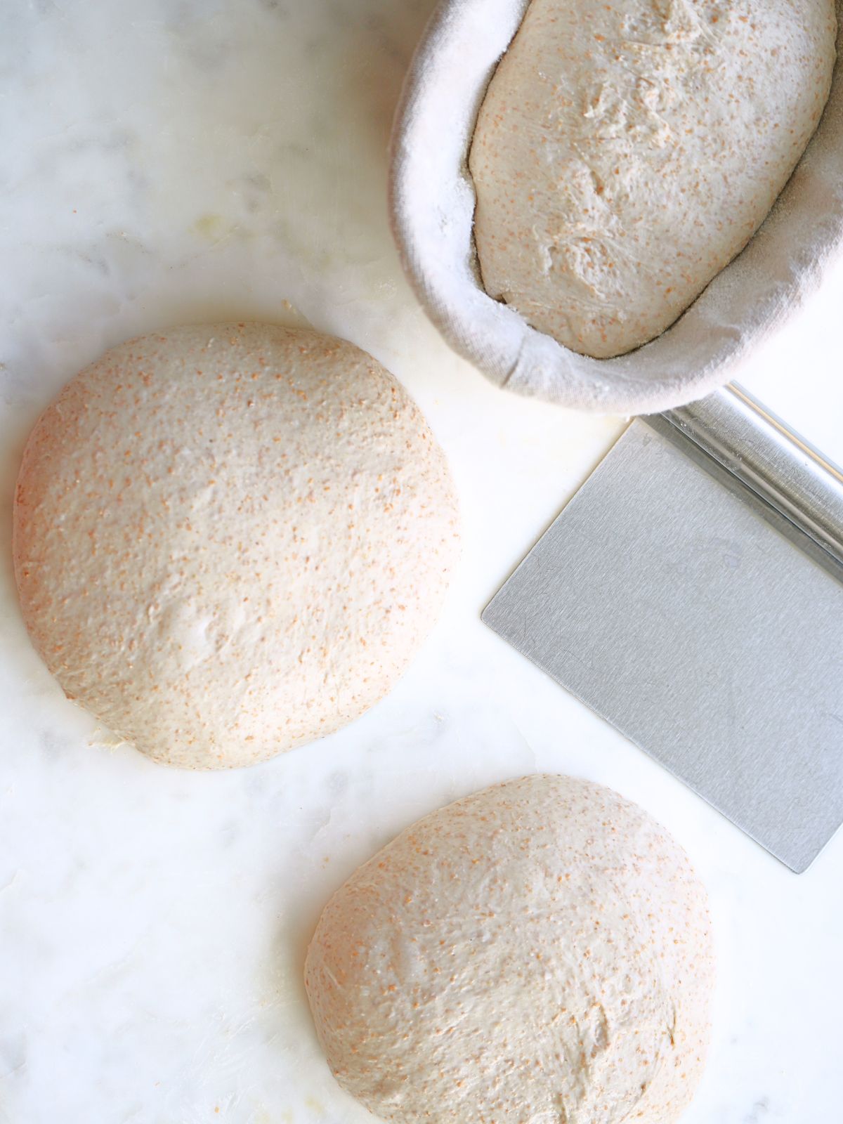 Dough in a basket and on the counter with a bench scraper.