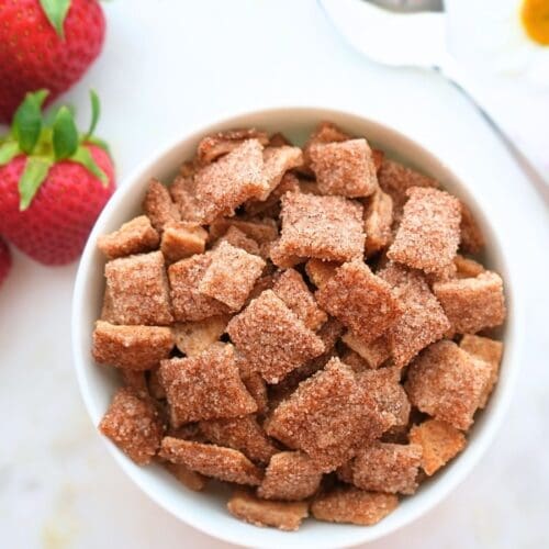 A bowl of sourdough discard Cinnamon Toast Crunch with berries, flowers, and a spoon on the counter.
