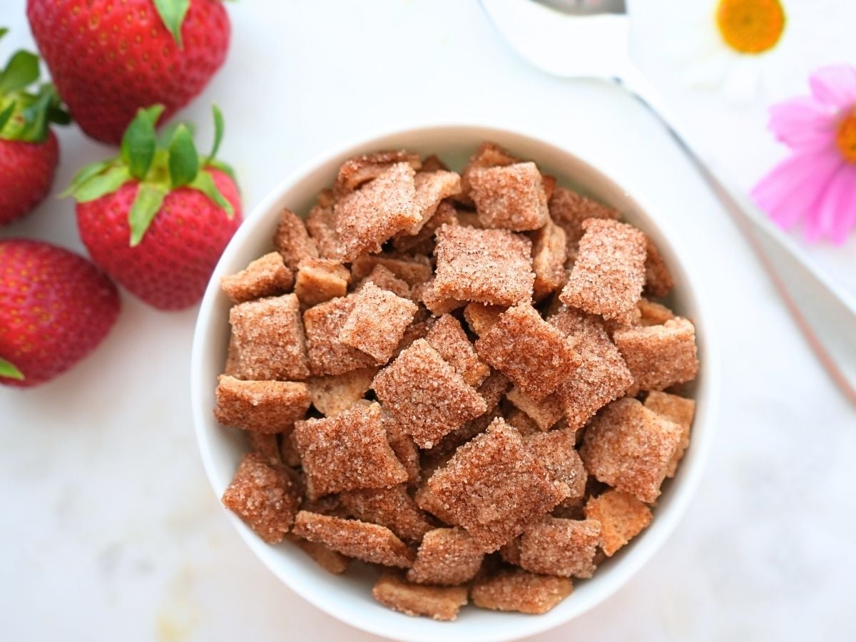 A bowl of sourdough discard Cinnamon Toast Crunch with berries, flowers, and a spoon on the counter.