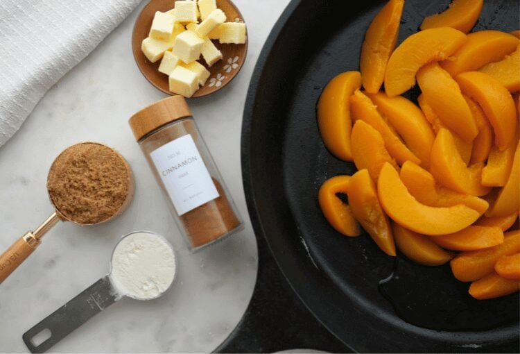 Peaches in a cast iron skillet, shown with flour, cinnamon, and butter