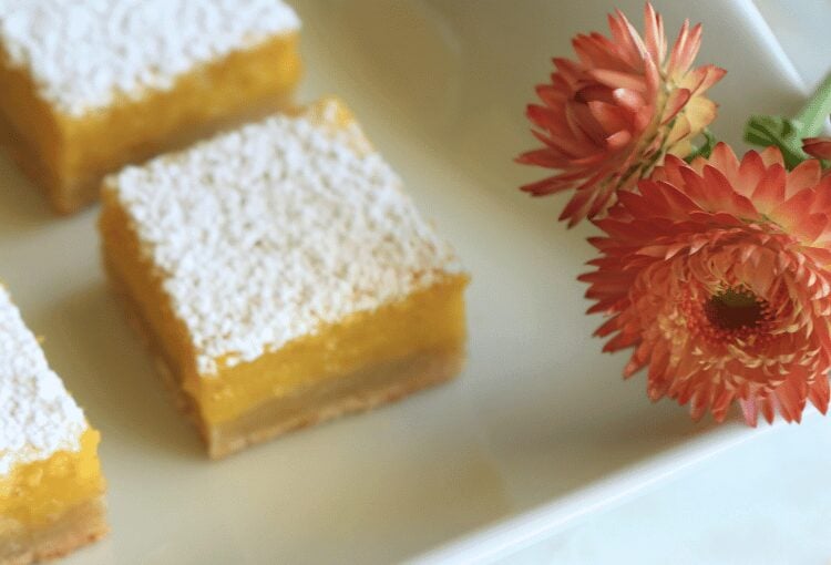 Lemon bar squares on white plate next to pink cut flowers
