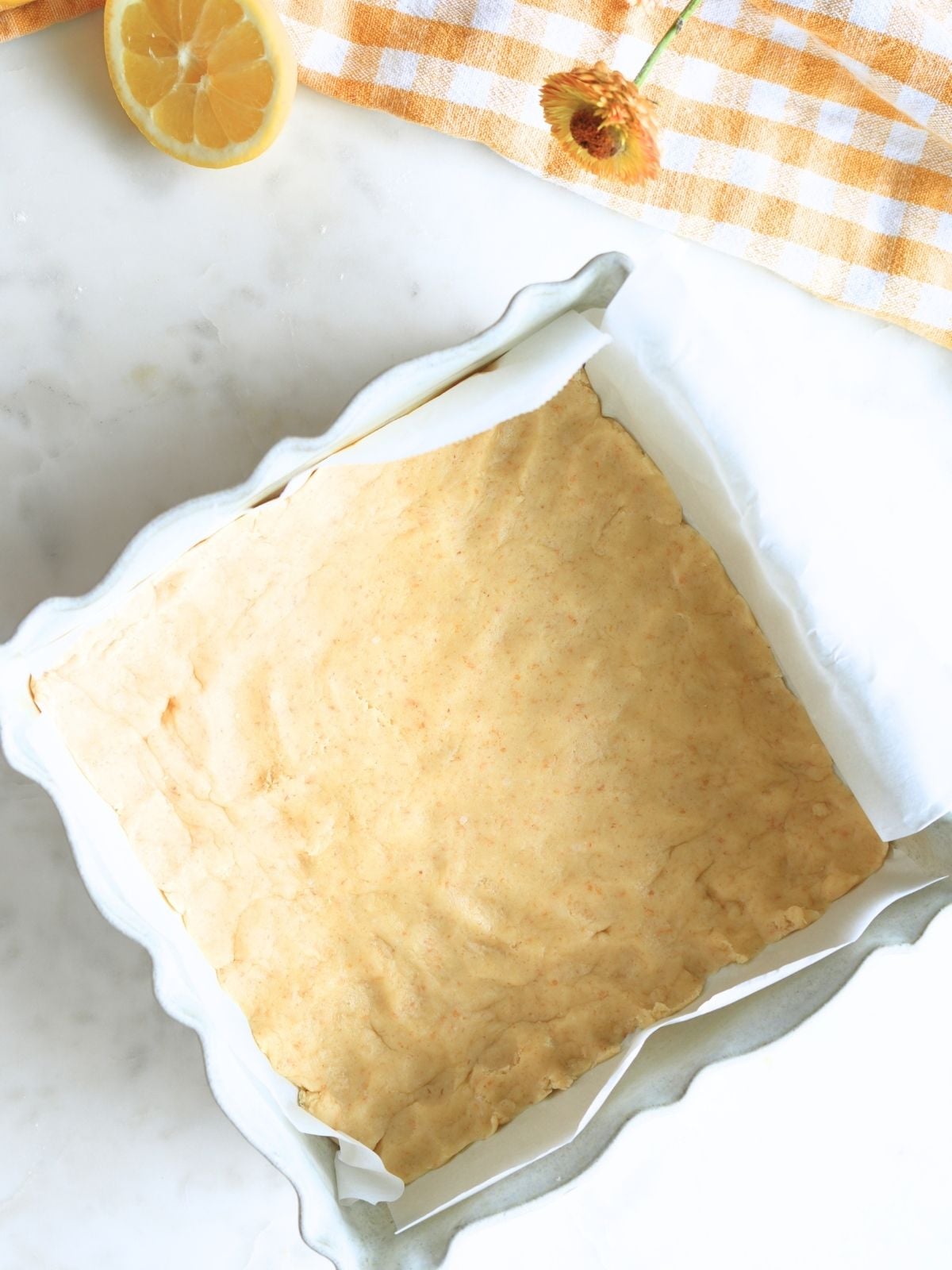 Lemon bar cookie base in a parchment-lined baking dish.