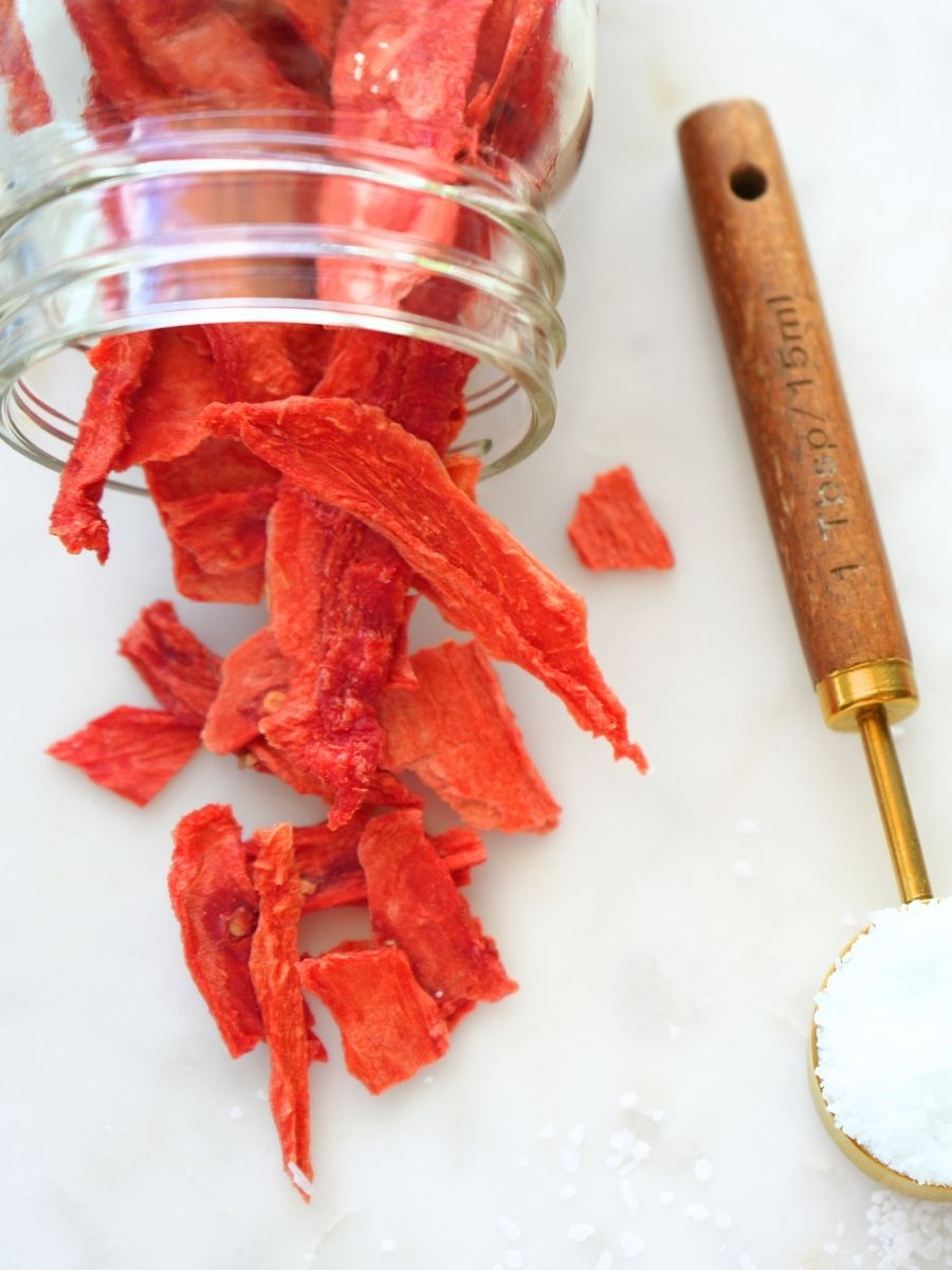 Dehydrated watermelon spilling out of a jar next to a tablespoon of salt