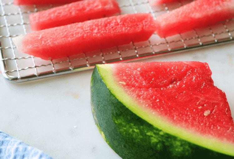 Sliced watermelon wedge with rectangular slices on dehydrator tray in the background