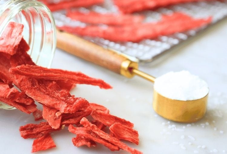 Dehydrated watermelon spilling onto a counter with salt and a tray of watermelon in the background