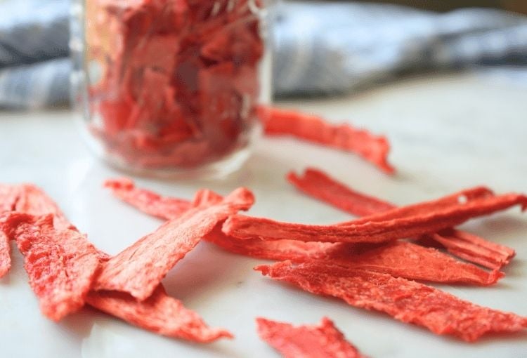 Watermelon jerky on a counter with a jar filled in the background