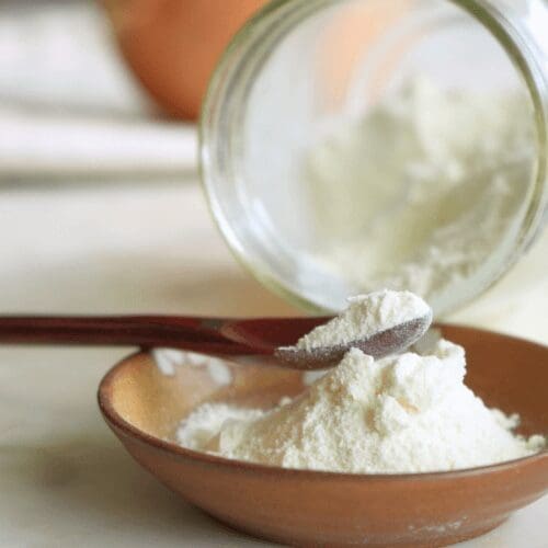 Freeze dried onion powder in glass mason jar pouring into small dish with wood spoon