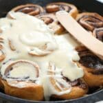 Partially iced sourdough pumpkin cinnamon rolls in a skillet.