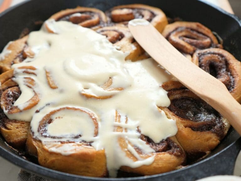 Partially iced sourdough pumpkin cinnamon rolls in a skillet.