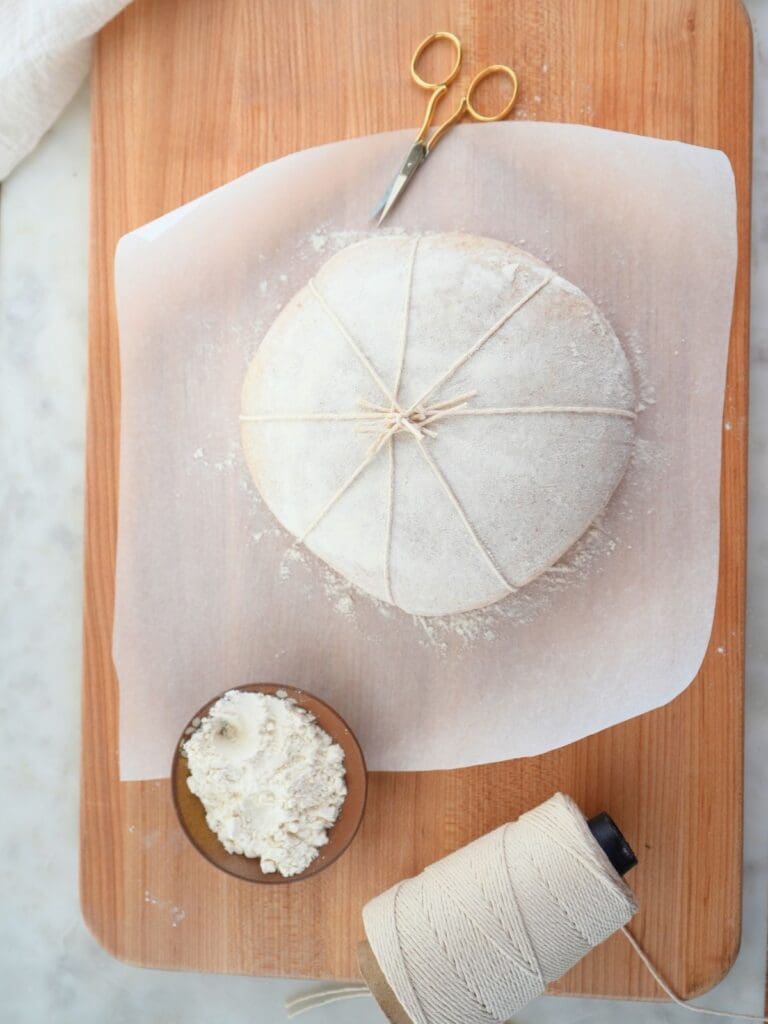 Sourdough dough with all the pieces of twine tied and knotted at the center of the dough. 