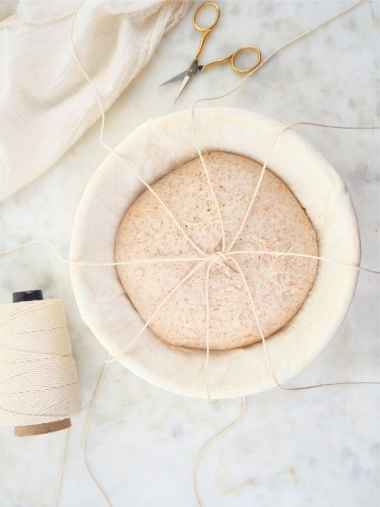 Sourdough dough with four pieces of twine spread across it.