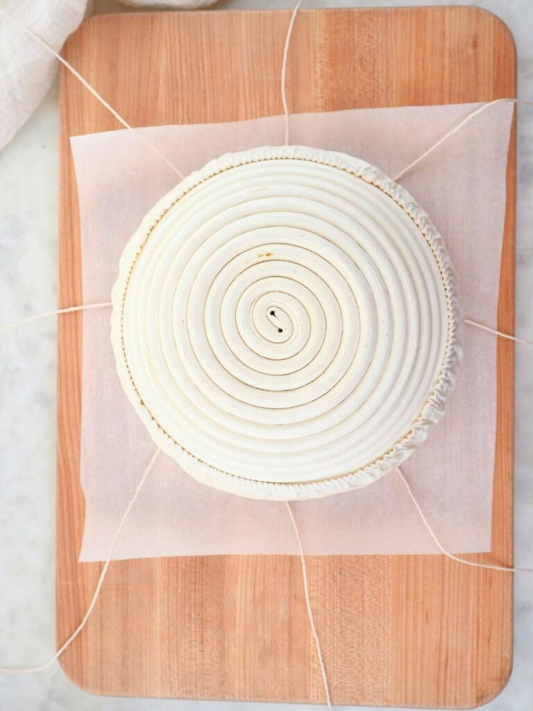 Banneton basket with parchment paper and a cutting board underneath it.