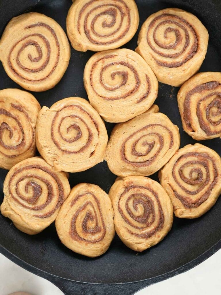 Unbaked sourdough pumpkin cinnamon rolls in a cast iron skillet.