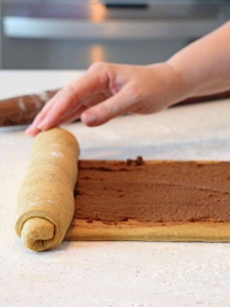 Sourdough pumpkin cinnamon roll dough being rolled into a log shape.