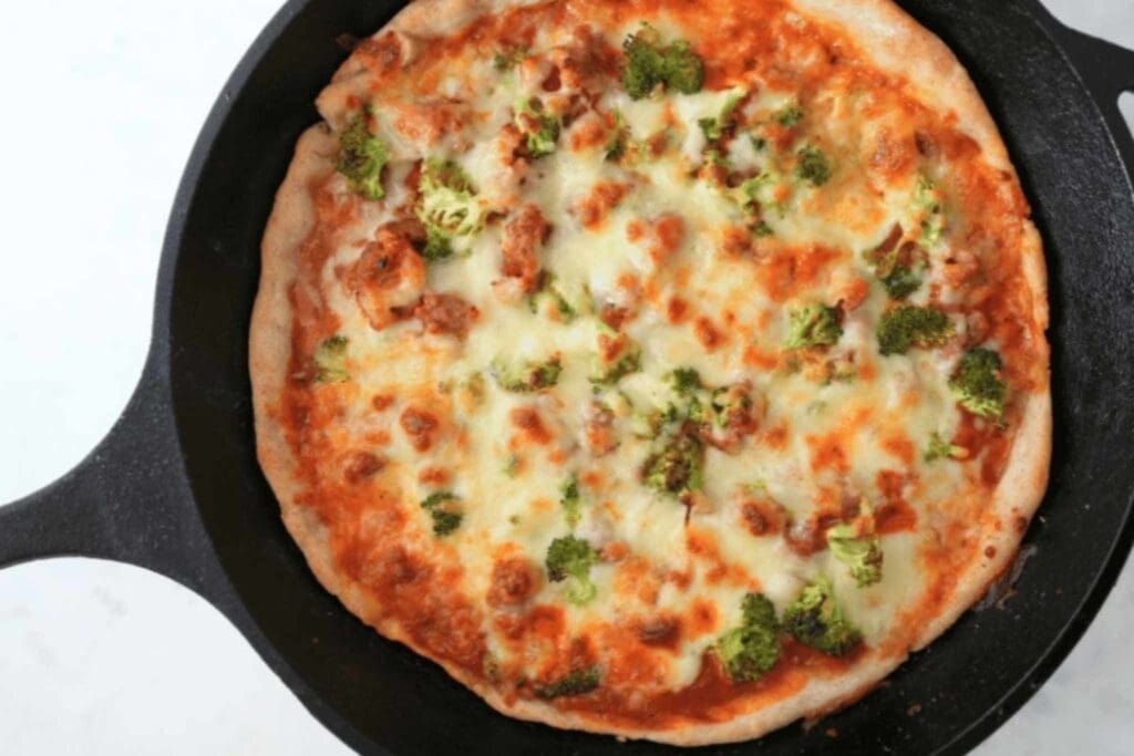 Pizza made with sourdough pizza dough in a cast iron skillet, topped with cheese and broccoli