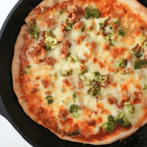 Pizza made with sourdough pizza dough in a cast iron skillet, topped with cheese and broccoli