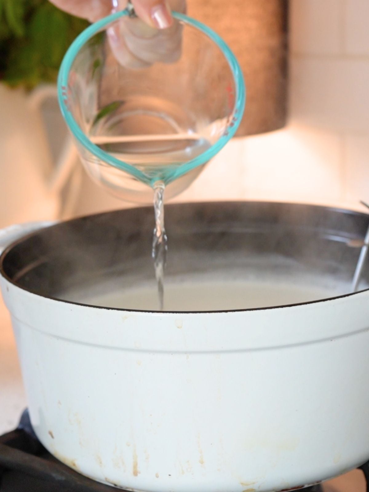 Vinegar being poured into a Dutch oven filled with warm milk.