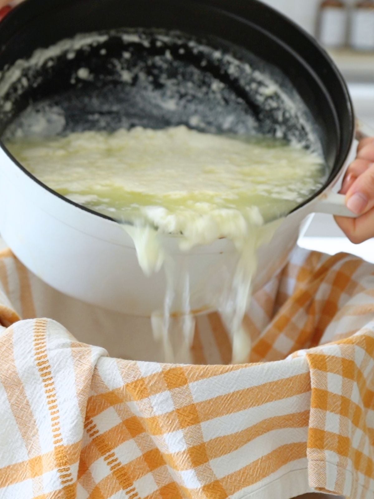 Curds and whey being poured into a towel-lined bowl.