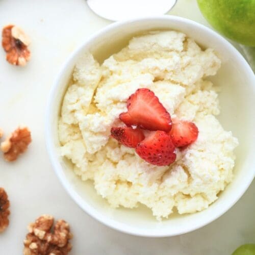 Small bowl of homemade cottage cheese with strawberries on top, shown with walnuts and grapes next to bowl