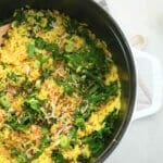 One pot turmeric coconut rice in a cast iron Dutch oven shown with wood serving spoon. and a halved lime
