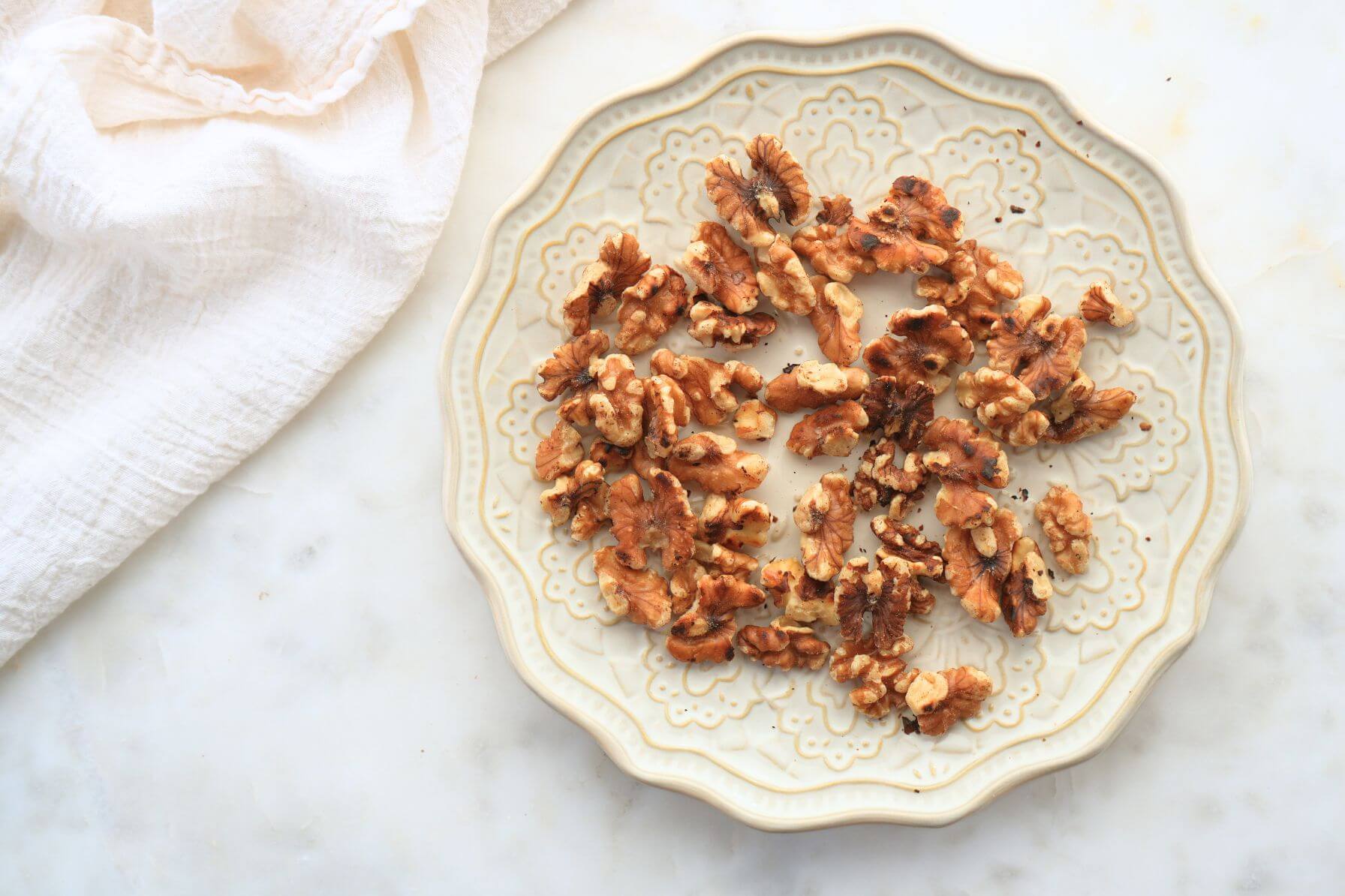 Toasted walnuts arranged on a decorative plate on a marble surface.