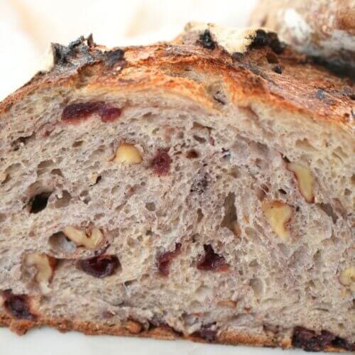 A boule of sourdough cranberry walnut bread sliced in half, showing the crumb