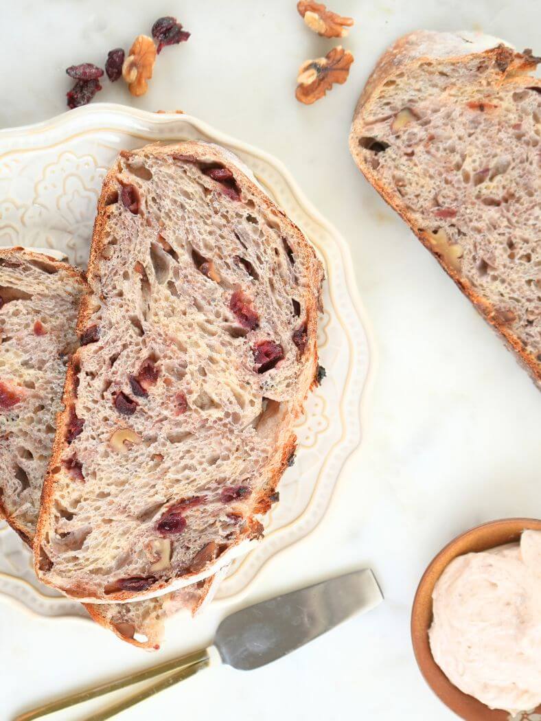 Sliced sourdough cranberry walnut bread on scattered on a plate and counter