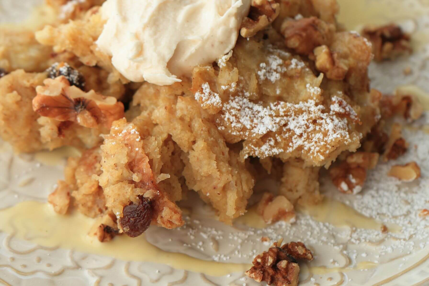 Side angle of sourdough bread pudding with golden raisins and whipped cream on a marble background.