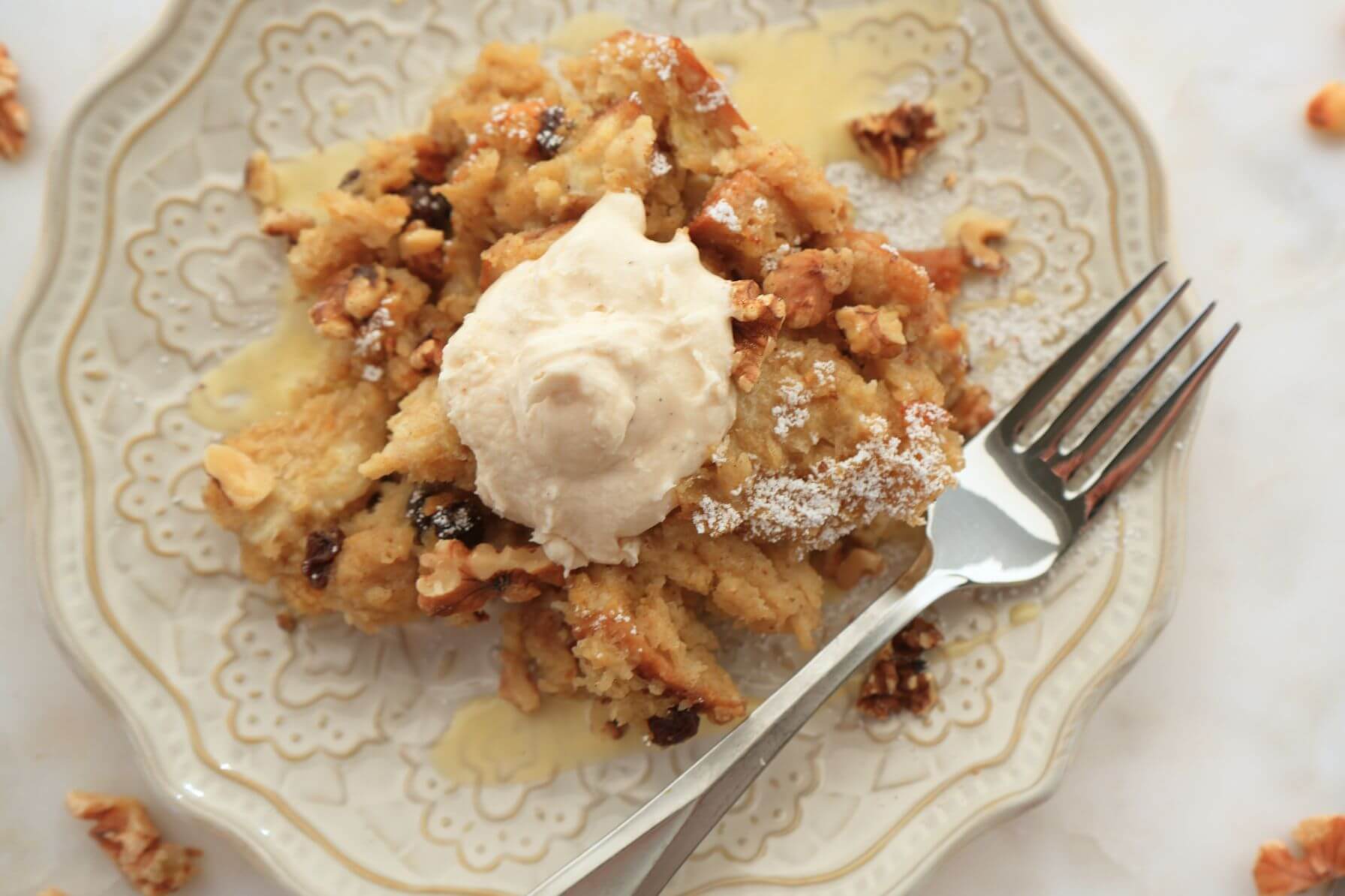 Bread pudding on a decorative plate with a drizzle of custard, topped with creamy whipped topping.
