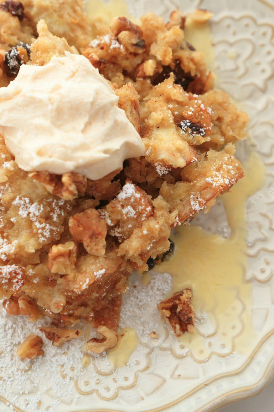 Detailed shot of a plate of bread pudding garnished with walnuts and a drizzle of egg nog on the plate.
