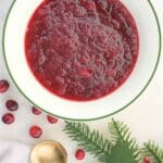 Homemade cranberry sauce in a bowl with fresh cranberries and greenery scattered